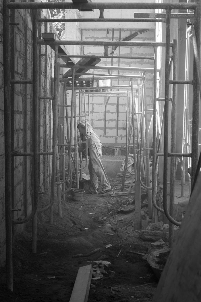 services-01 A lone worker amidst scaffolding in a dimly lit construction site.