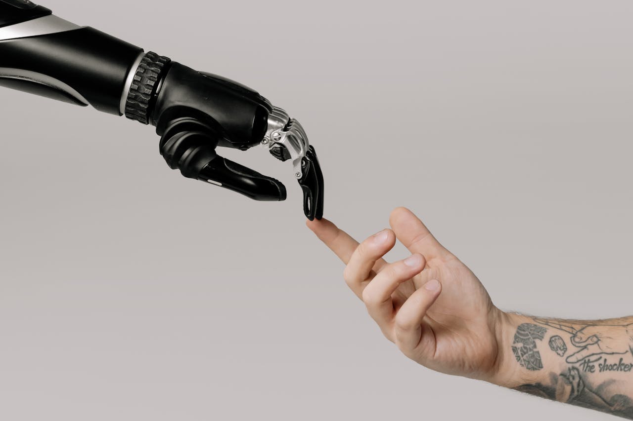 about-02 A human hand with tattoos reaching out to a robotic hand on a white background.