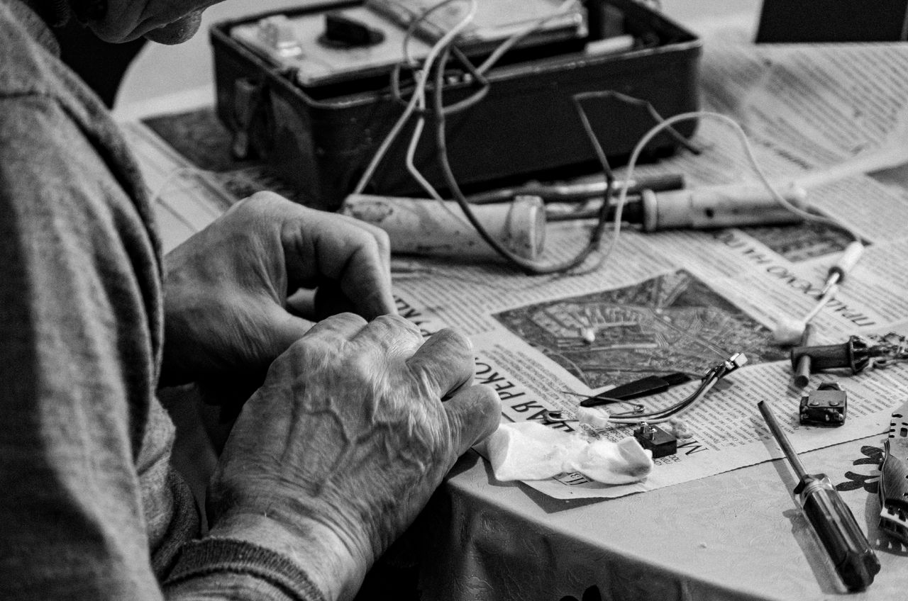 services-04 Monochrome close-up of hands repairing an electronic device on a table.