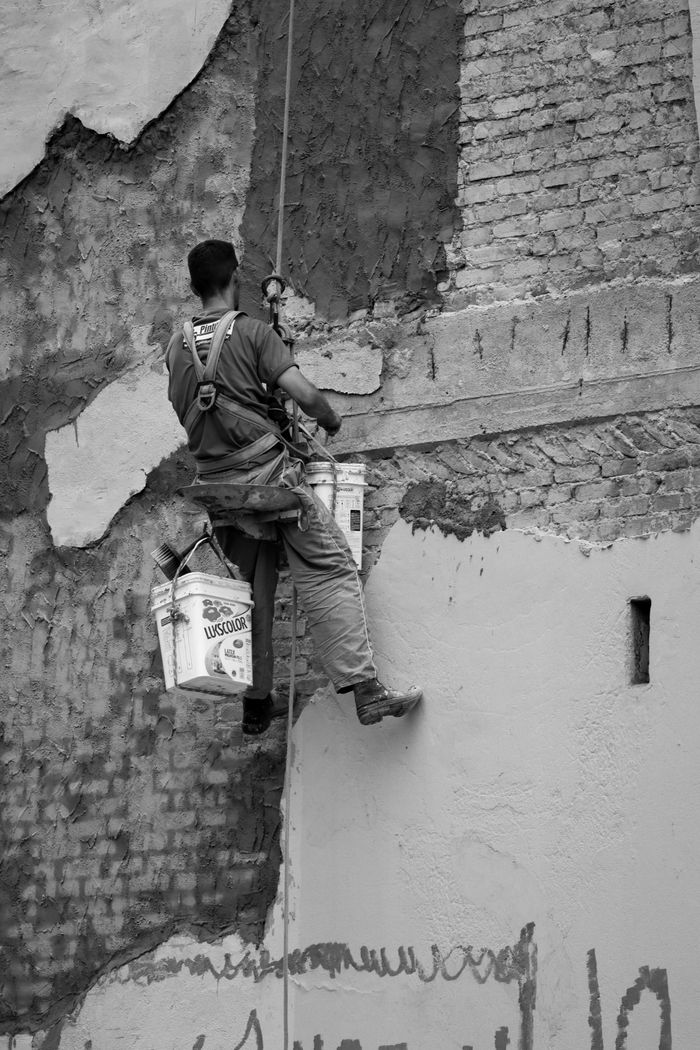 contact-img Black and white photo of a worker on a rope restoring a wall.