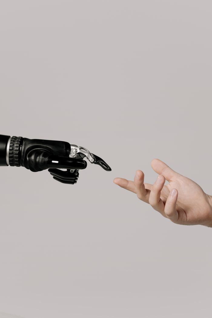 services-02 A human hand reaching to touch a bionic prosthetic hand on a white background.